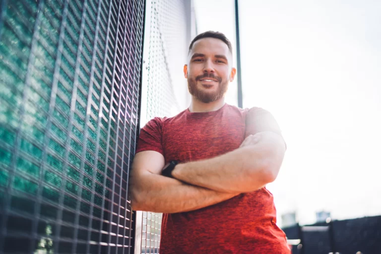 cheerful sportsman standing against fence utc